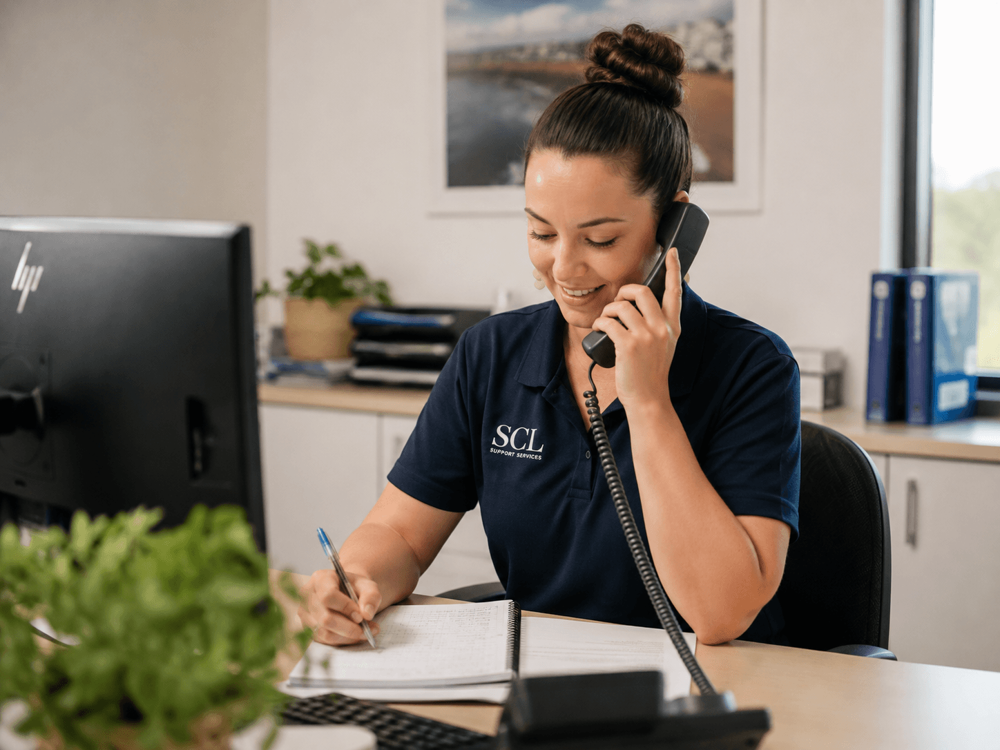 Office administration team member taking a phone call and making notes.